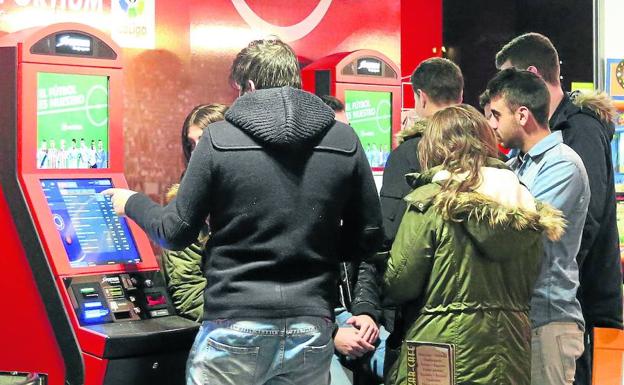 Un grupo de jóvenes realiza una apuesta deportiva en una máquina de un salón de juegos.