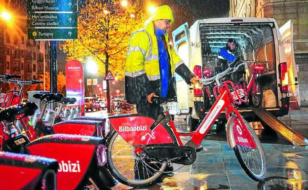 Un operario repone varias bicicletas eléctricas en el punto de anclaje próximo al Ayuntamiento bajo un intenso aguacero.