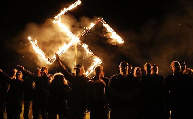 Neonazis estadounidenses hacen el saludo fascista delante de una cruz gamada en llamas en Virginia (EE UU).