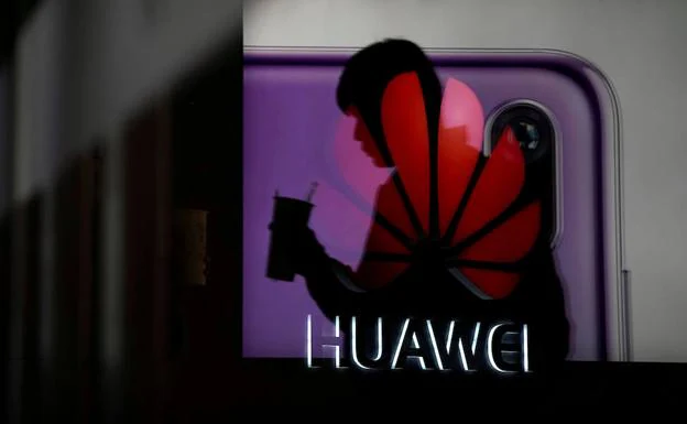 Un hombre camina frente a una puerta de cristal en la que se refleja el logotipo de Huawei, en un centro comercial de Shanghái.