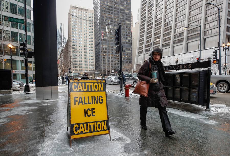 Una persona camina por las calles de Chicago junto a un cartel que advierte del peligro de caídas de hielo de los edificios