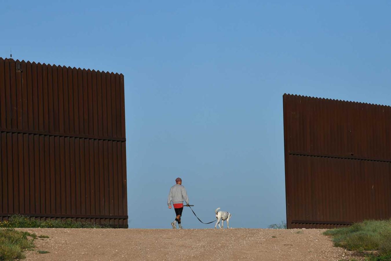 Hombre paseando a su perro por un tramo de cerca fronteriza en el Valle del Río Grande cerca de Penitas, Texas