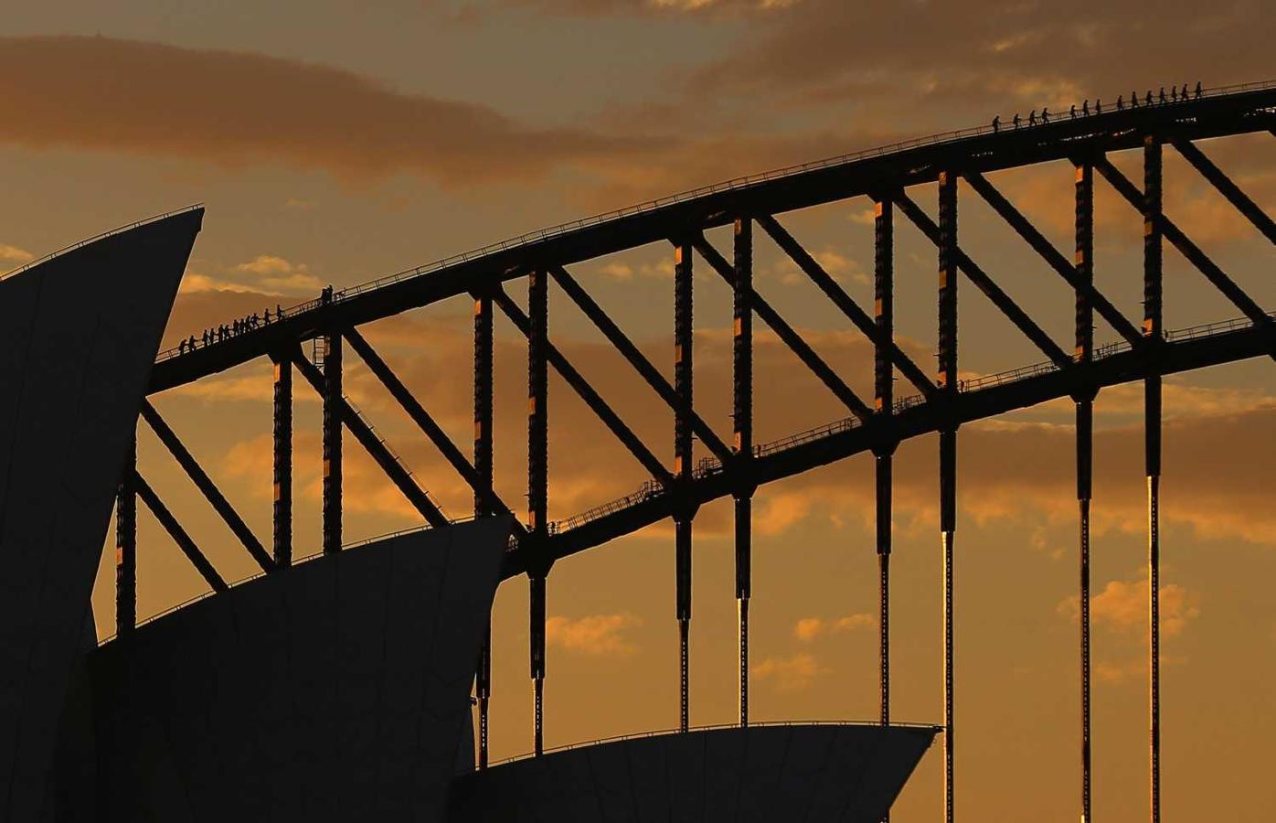 Escaladores ascienden el arco del puente sobre la bahía de Sídney frente a la Casa de la Ópera este lunes en Sídney, Australia