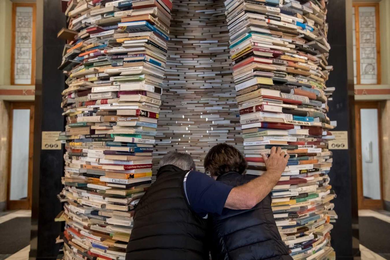 Dos personas observan la escultura titulada "Idioma" del artista eslovaco Matej Kren, una columna hecha de 8.000 libros, expuesta en la entrada de la Biblioteca Central de Praga (República Checa) durante la celebración del Día del Libro