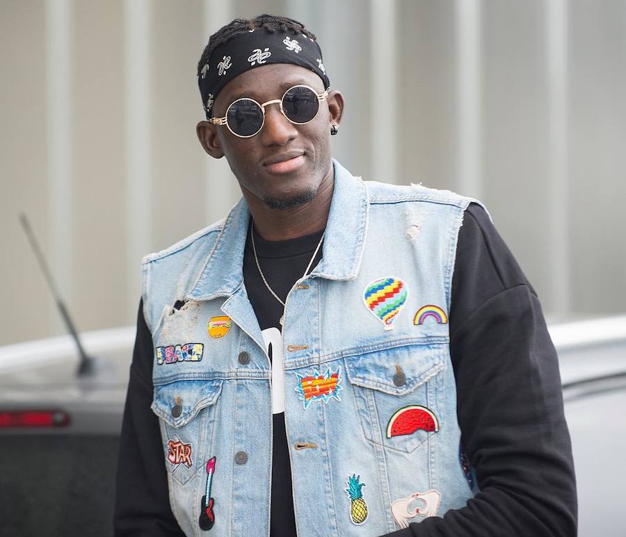 Diop con bandana a la cabeza, gafas de sol con montura dorada y un llamativo chaleco vaquero repleto de parches multicolor.