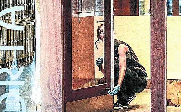 Una agente de la Ertzaintza científica busca huellas en la puerta del portal donde se produjo el asalto.