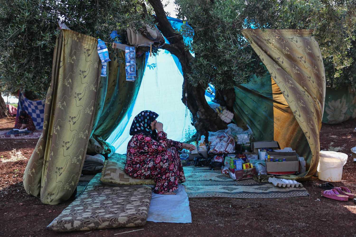 Una mujer se sienta a la sombra de un árbol en un campamento para personas desplazadas en la aldea de Atme, Siria 