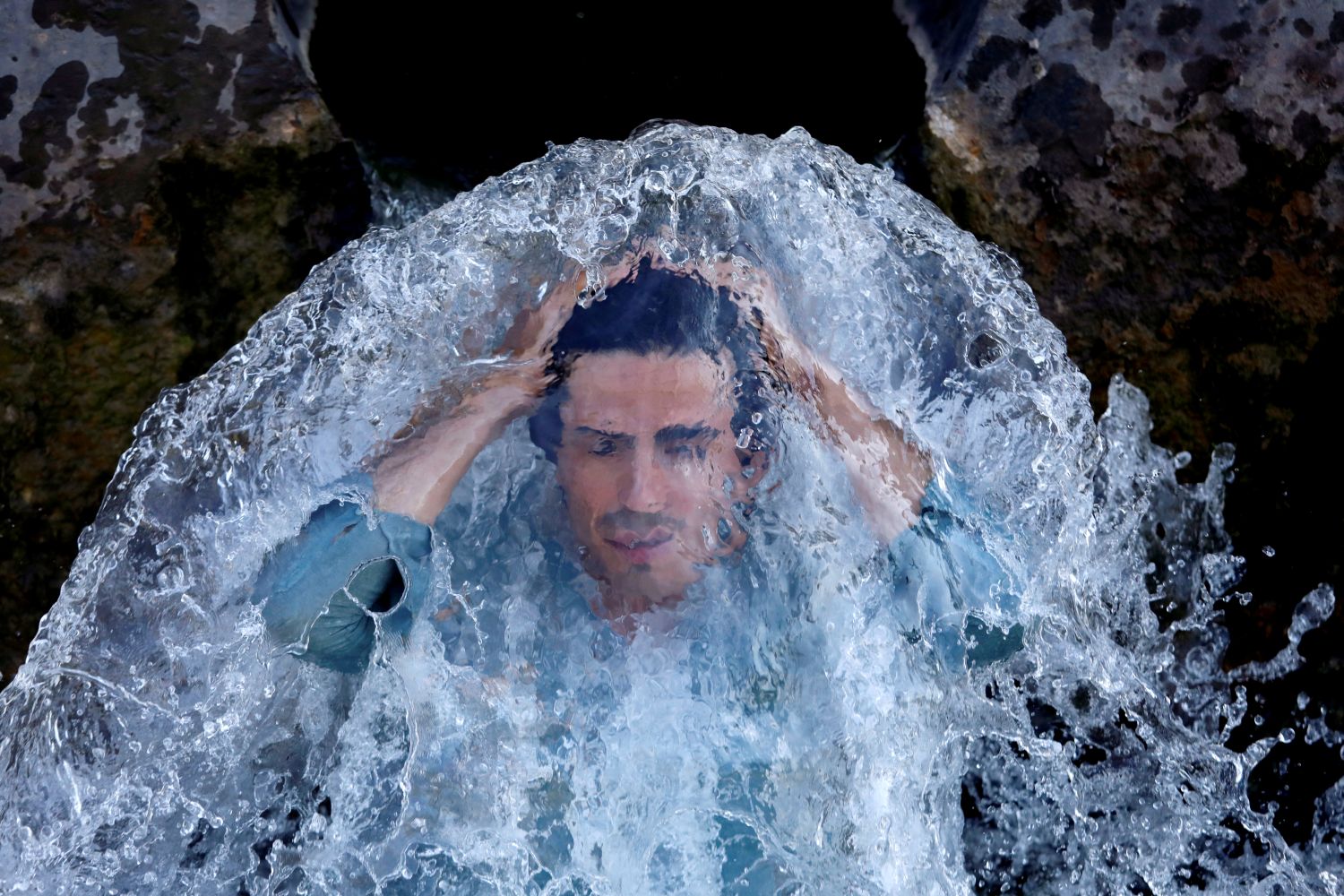 Un hombre se refresca bajo una tubería de agua de un canal en las afueras de Peshawar, Pakistán.