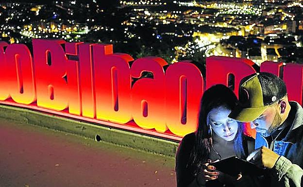 Una pareja se conecta a la tablet para hacer una consulta en el mirador de Artxanda, con Bilbao a sus pies.