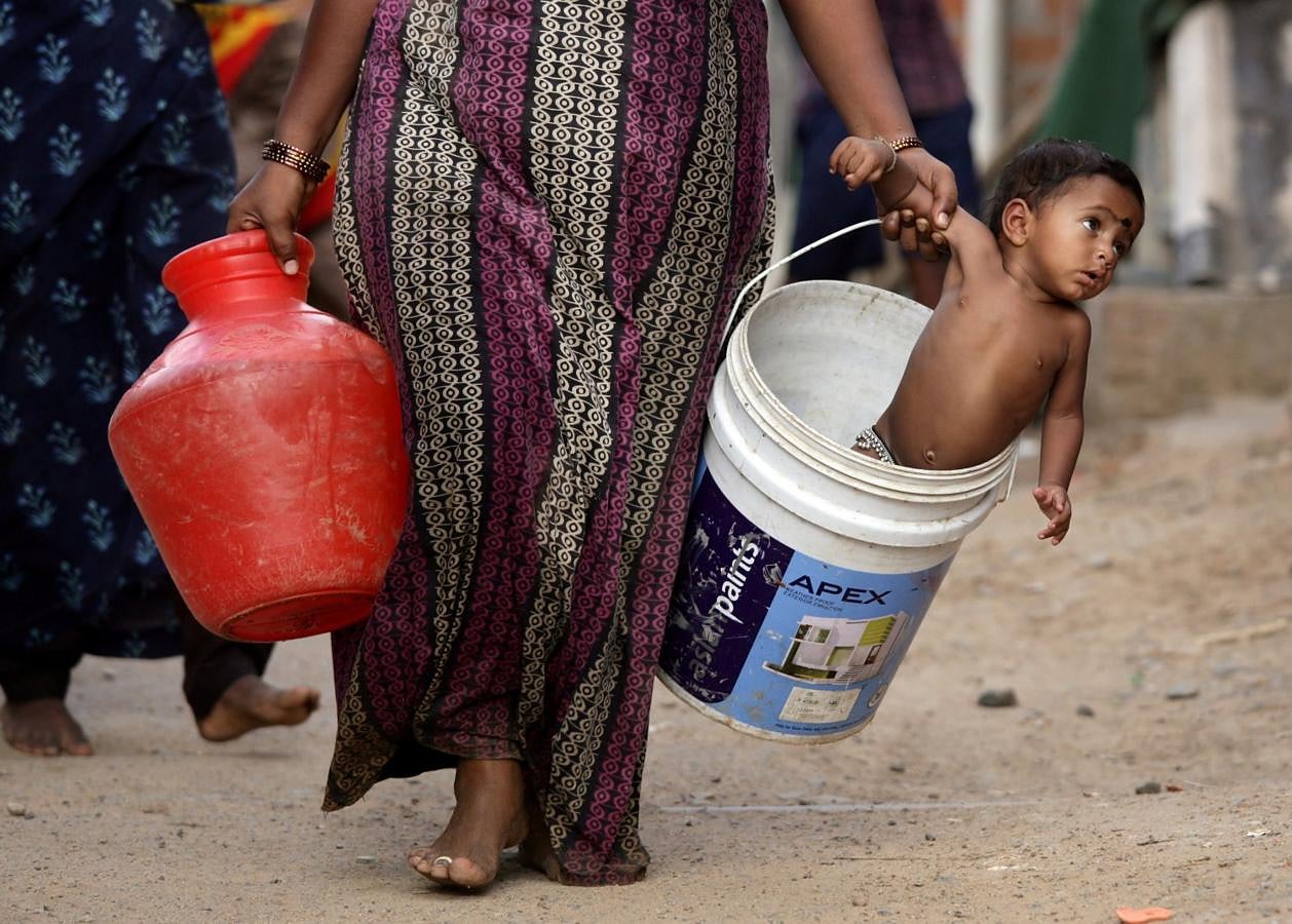 Una mujer lleva a su hijo en un balde después de recoger agua de un camión cisterna municipal en las afueras de Chennai, India