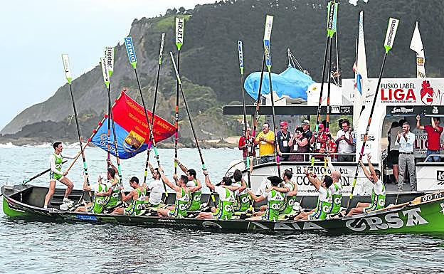 El patrón de Hondarribia, Joseba Amunarriz, ondea la Ikurriña de Ondarroa, mientras su tripulación alza los remos.