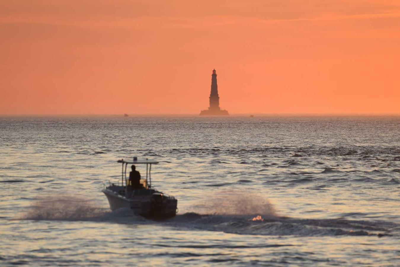 Un barco navega al atardecer frente a la costa de Le Verdon-sur-Mer, en el suroeste de Francia, con el faro de Cordouan al fondo