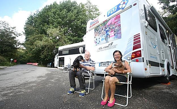 Dos aficionados esperan con sus perros la llegada de los ciclistas.