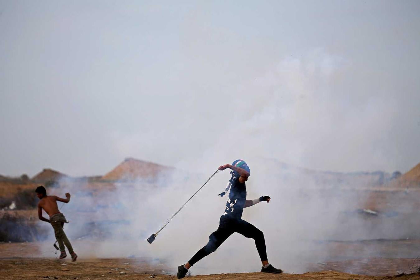 Manifestante palestino con una honda para arrojar un bote de gas lacrimógeno en la frontera entre Israel y Gaza