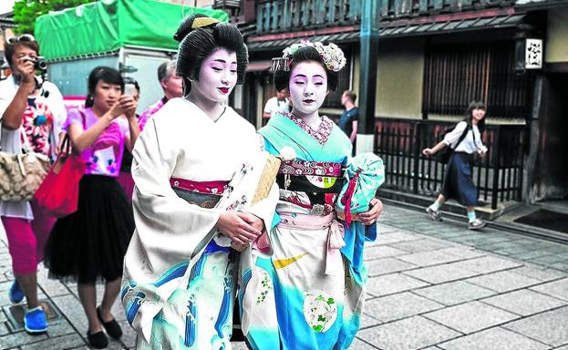 Dos geishas caminan por una callejuela de Kioto perseguidas por varios turistas que las fotografían.