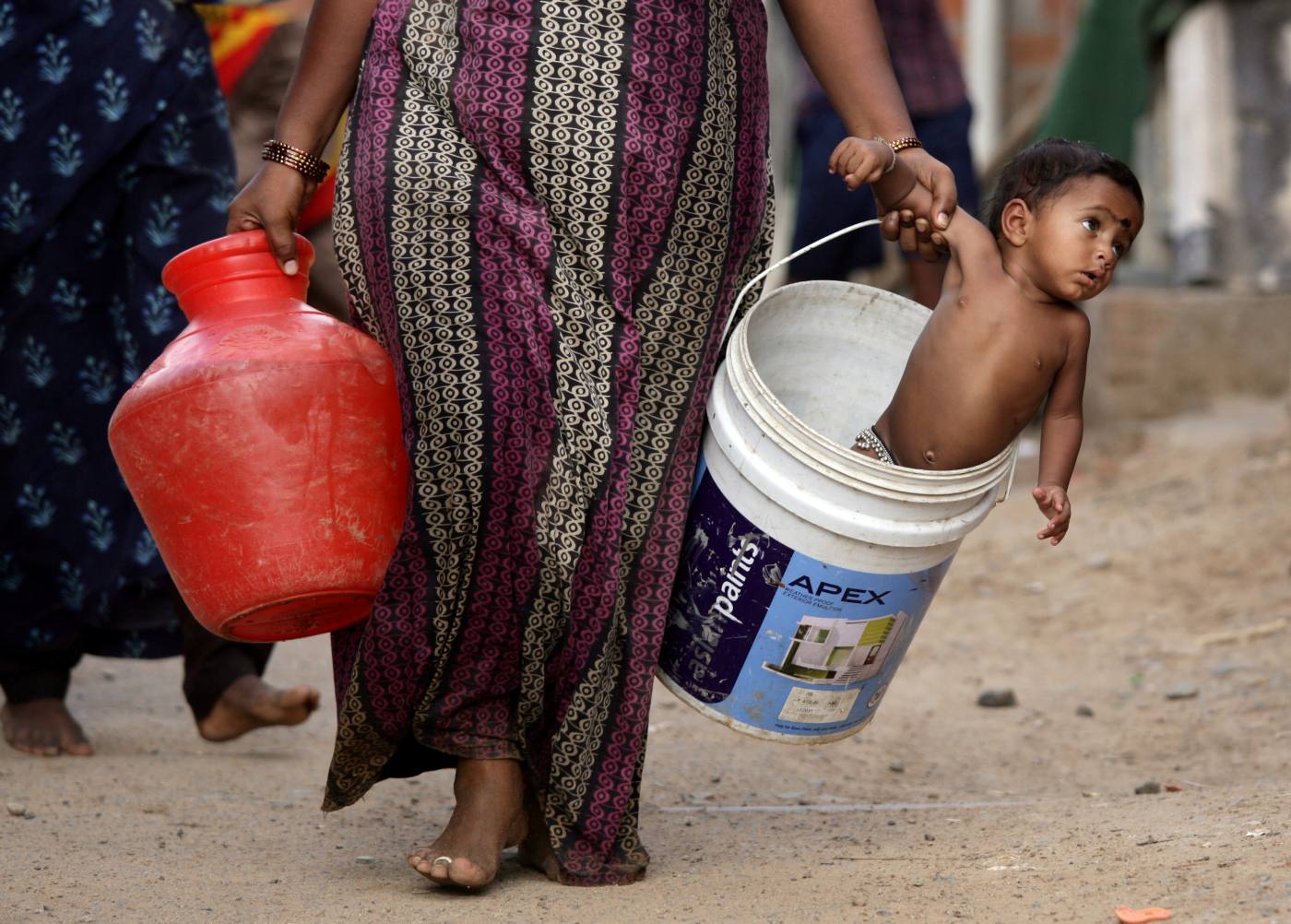 Una mujer transporta a su bebé en un cubo después de coger agua de un tanque municipal a las afueras de Chennai, en India.