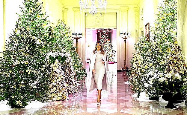 Melania Trump camina por el Cross Hall, donde ha 'plantado' varios pinos naturales adornados con nieve artificial y dorados. 