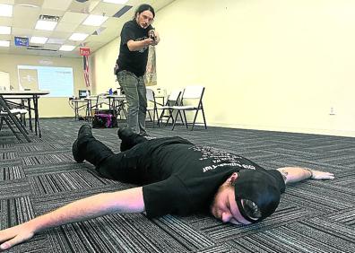 Imagen secundaria 1 - Arriba, una de las últimas 'promociones' de 'agentes de recuperación de fianzas' que han obtenido el certificado en el 'bootcamp' que Gribbles posee en el Estado de Washington, tras un cursillo de 48 horas. A la izquierda, un alumno encañona a otro durante una clase práctica. A la derecha, una agente del equipo de Gribbles conduce a una mujer esposada, acusada de maltratar a su hijo, a un presidio del condado de Kootenia, en Idaho.