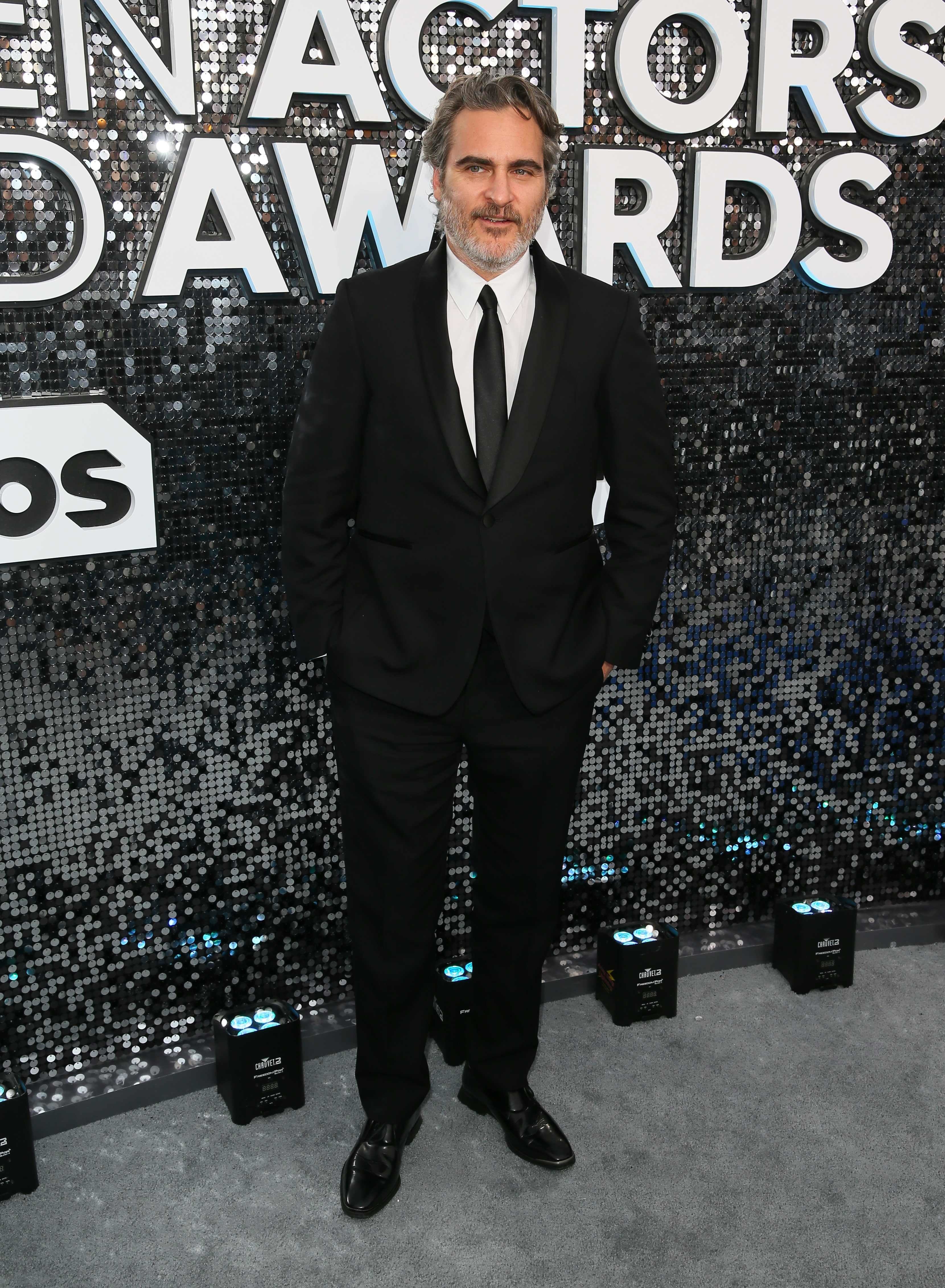 Joaquin Phoenix con un traje de chaqueta negro y corbata a tono, de Stella McCartney.