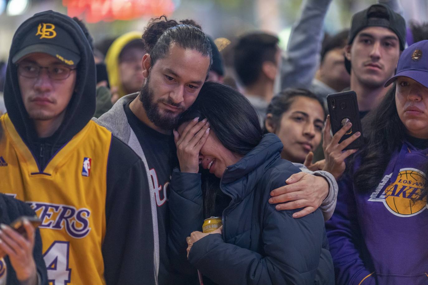 Una pareja de aficionados se abraza junto al improvisado altar a Kobe Bryant en la plaza del Staples Center en Los Ángeles.