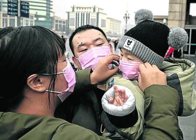 Imagen secundaria 1 - En China se extienden los controles en los servicios de transporte y vehículos privados. Unos padres colocan la mascarilla a su hijo en una calle de Pekín. Un hombre baja de una ambulancia en Wuhan.