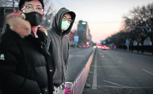 Dos jóvenes protegidos con máscaras se disponen a cruzar una carretera, prácticamente desierta, en la capital, Pekín.