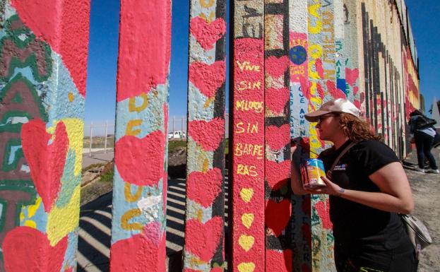 Una mujer pinta corazones en la valla fronteriza de EE UU y México.