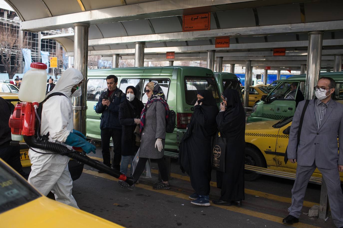 Un hombre desinfecta taxis frente a una estación en Teherán.