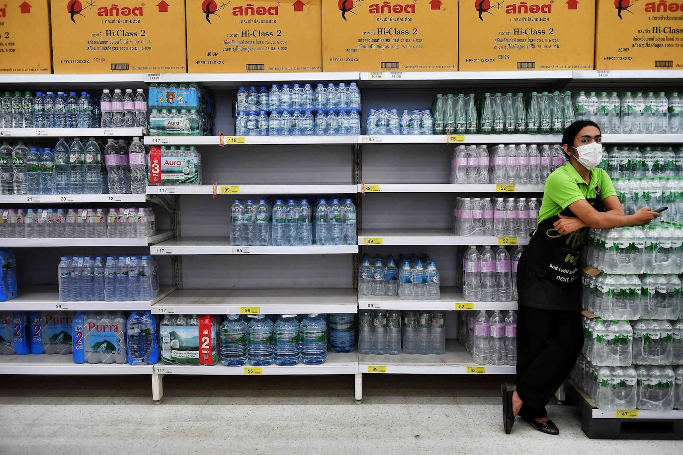 Una empleada, con una máscara por miedo al coronavirus, se detiene frente a los estantes de agua embotellada en un supermercado en Bangkok.