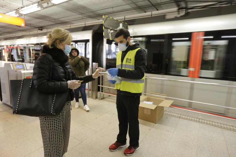 Un voluntario de la DYA entrega mascarillas a la entrada de la estación de La Arenas.