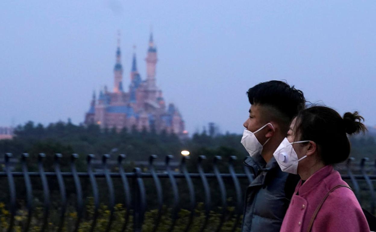 Ciudadanos chinos pasean rente al parque de atracciones de Disney en Shanghái, cerrado por el Covid-19.