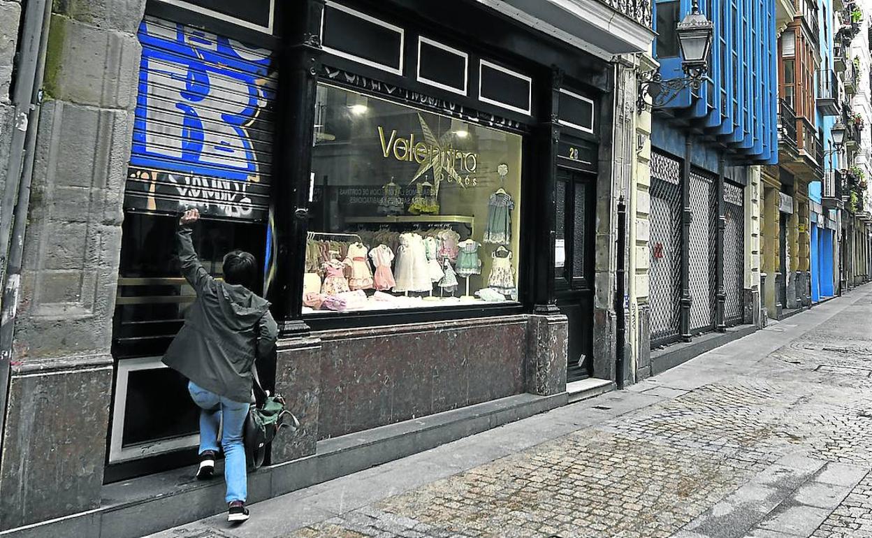Una mujer baja la presiana de su tienda de ropa situada en una calle del Casco Viejo de Bilbao.