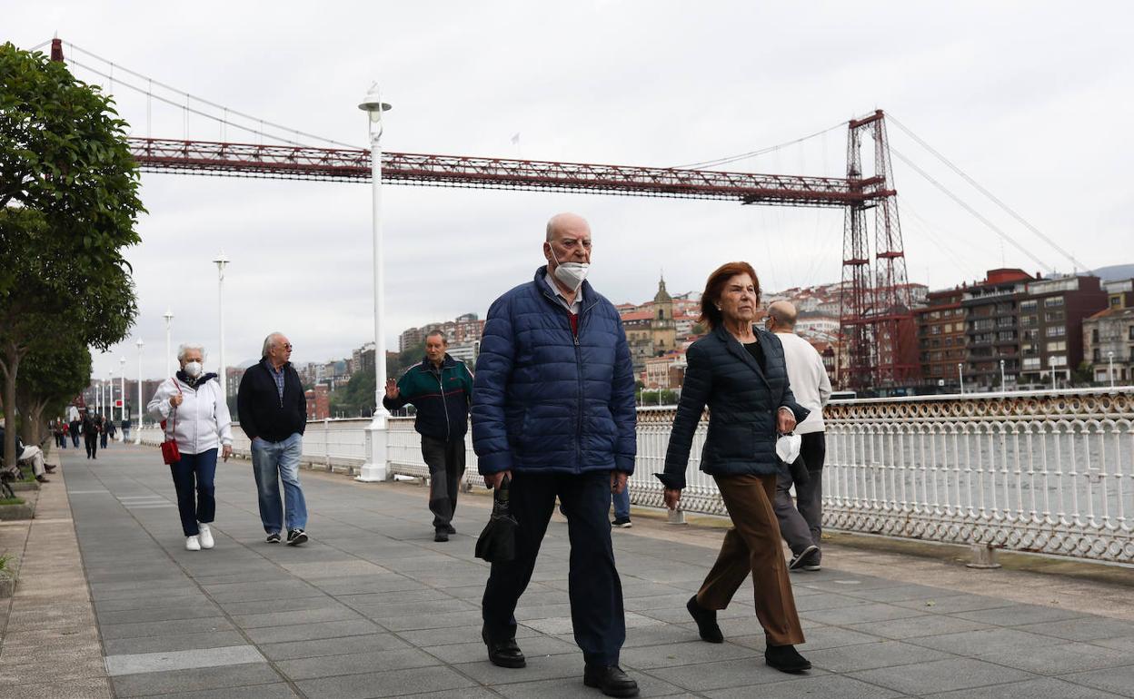 Varias personas pasean por Getxo con el Puente Colgante de testigo.