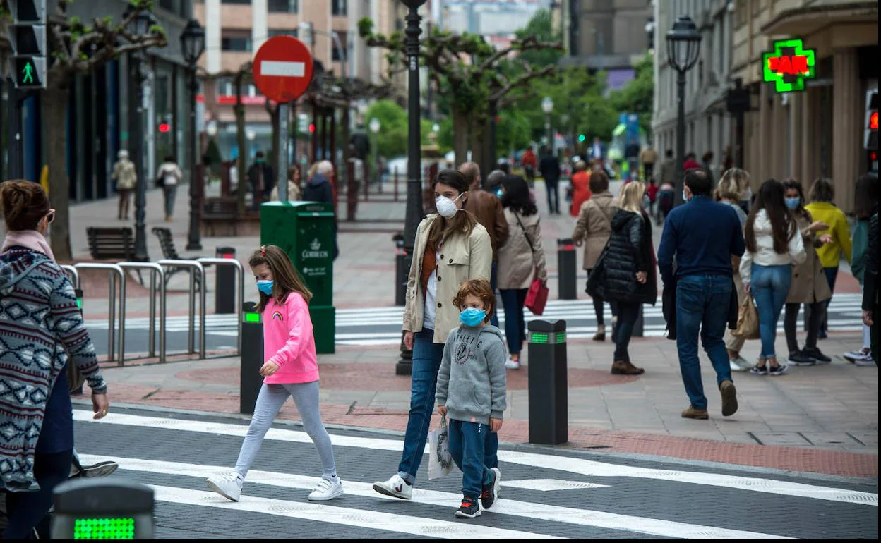 Una madre y sus dos hijos, con mascarilla, cruzan un paso de cebra en Bilbao. 