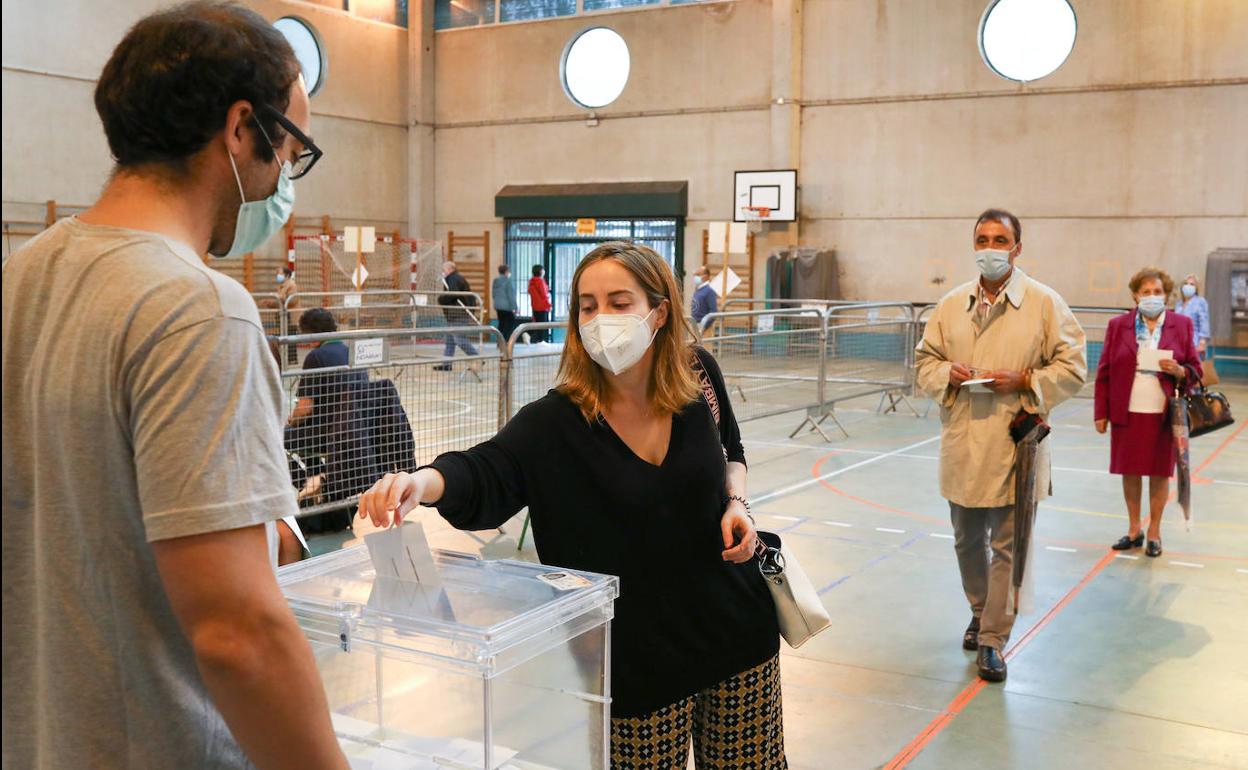 Una mujer deposita su voto tras en un colegio de Romo, mientras varias personas hacen cola para votar.