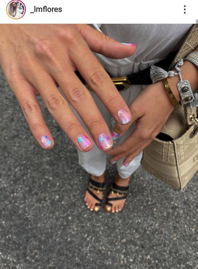 También estarán muy presentes este tipo de manicuras que nos recuerdan mucho a nuestra infancia. Diseños como este de Laura Matamoros con fondo rosa claro, estrellas de colores y brillo son una buena opción para este verano.