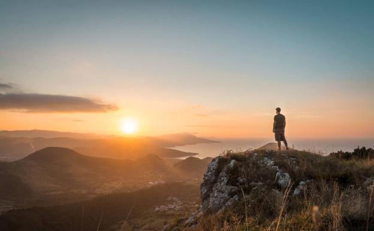 Un hombre observa cómo el sol se pone sobre el mar desde las estribaciones del Serantes.