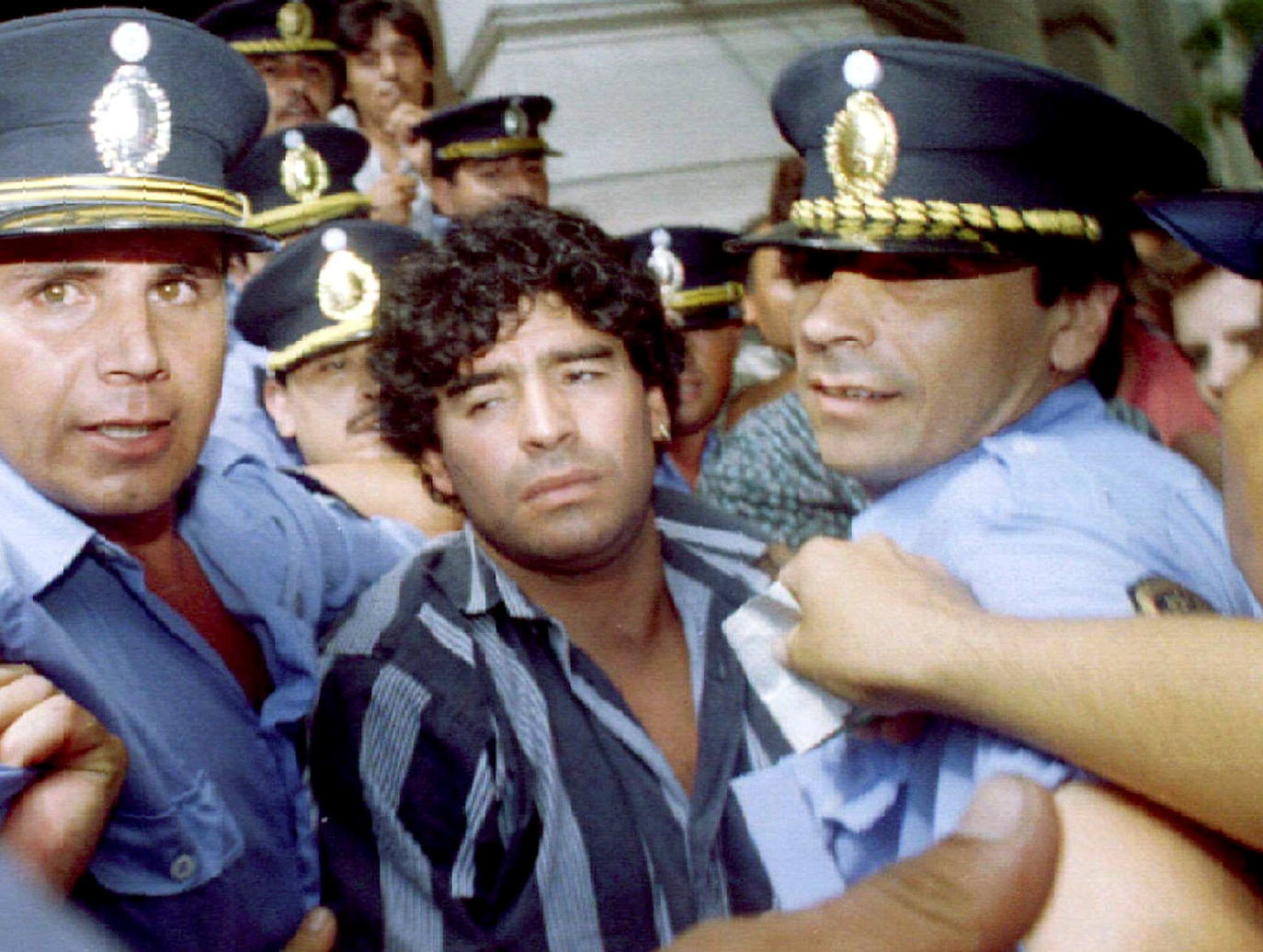 Maradona escoltado por la policía cuando sale de un juzgado después de responder a los cargos de que disparó e hirió a periodistas afuera de su casa de campo dos meses antes.