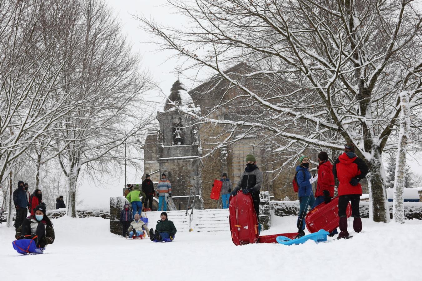 La gente disfruta de la nieve junto a la iglesia de Urkiola.