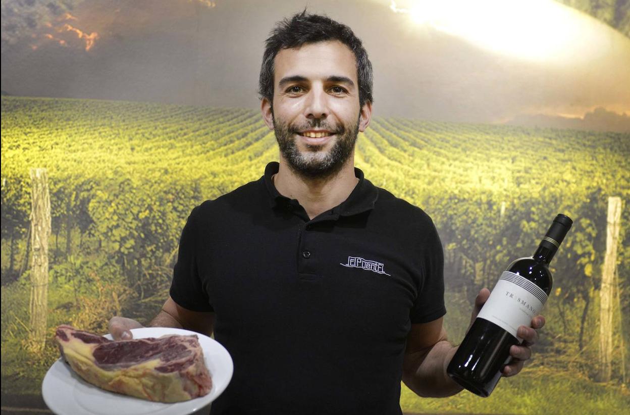 Jorge Lomas sostiene una chuleta y una botella de vino.