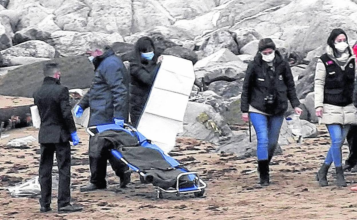 Empleados de una funeraria trasladan los restos mortales hallados en la playa de Arrigunaga, en Getxo, en presencia de agentes de la Ertzaintza. 