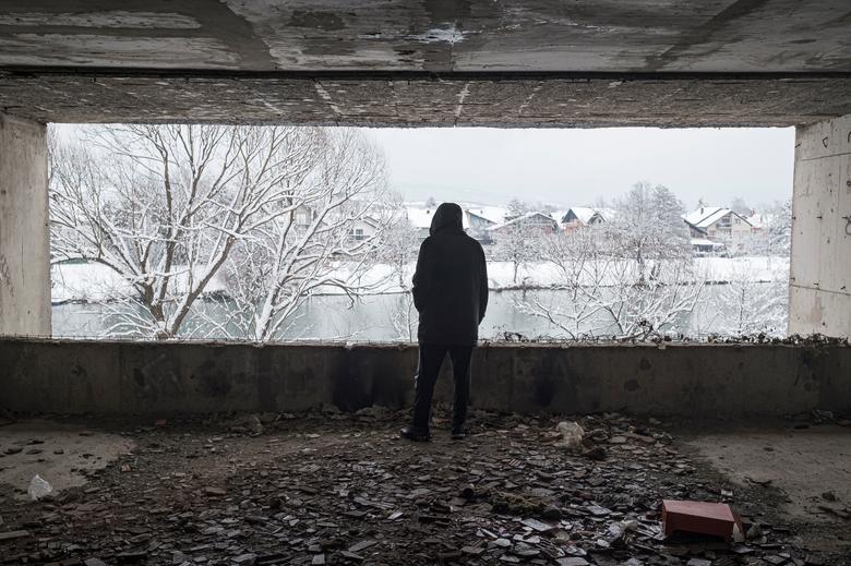 Un hombre mira por la ventana del edificio abandonado donde se alojan.