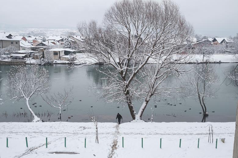 Un migrante lleva agua cerca de un edificio abandonado donde se encuentra en cuclillas.