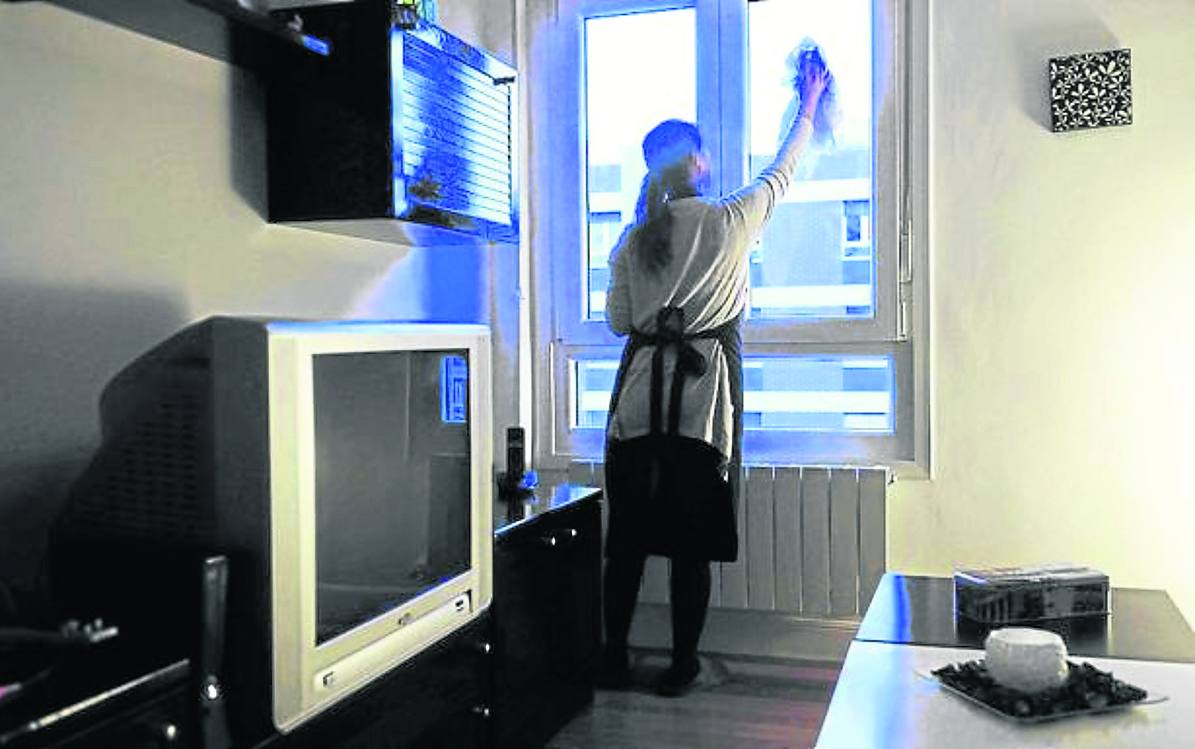 Una empleada del hogar limpia la ventana de la casa en la que trabaja.