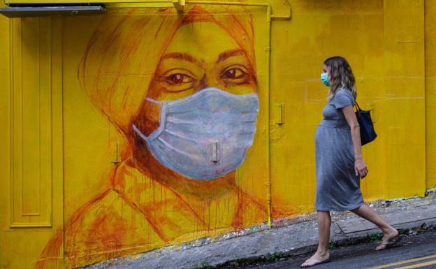Una embarazada camina por una calle de Hong Kong, delante de un mural callejero. 