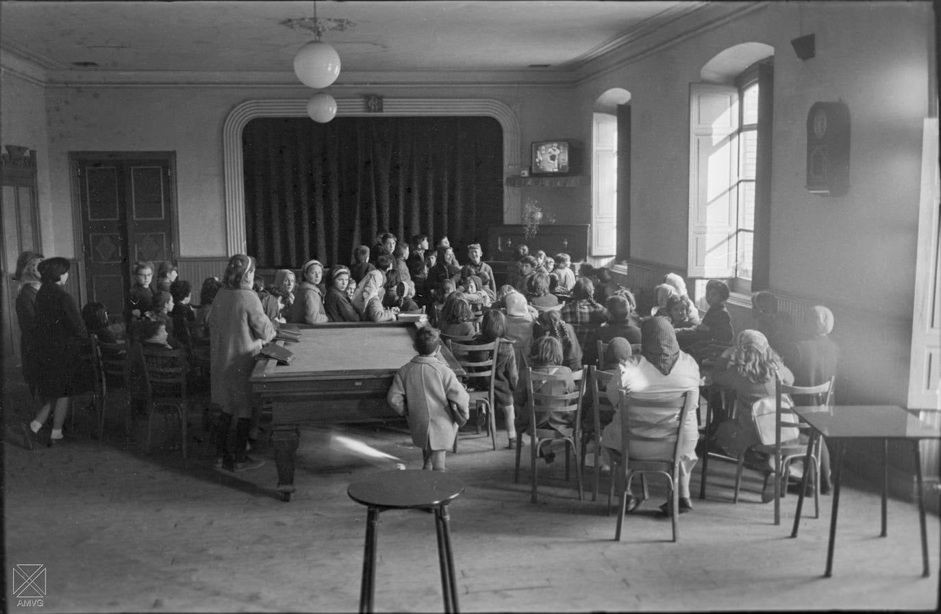 Tuvo Araya durante décadas un casino de postín. Antes de que se quemara en 1968, en su ‘reservado’ se jugaban los hombres las perras, se bailaba con la reconocida banda de música sin distinción de clases sociales, aunque la hubiera pues se movía dinero en el municipio gracias a la boyante siderurgia de Ajuria y Urigoitia; y se pasaba el rato con obras de teatro y comedias para todos los públicos en su pequeño escenario. Decorado con gusto exquisito, el salón tenía piano y billar, hasta que llegó al pueblo ese invento que fue la televisión y montaron una en una esquina. Quiere recordar el popular ‘Pinttu’ que al inicio de los años 60 se instalaron los tres primeros televisores en la próspera localidad, el del círculo recreativo, otro en casa del médico, un tal Guelbenzu, y un tercero en el bar Alegría, el de su familia, donde se agolpaba la gente a ver Bonanza. Todos los vecinos eran socios del casino y su biblioteca, como también de la Cooperativa de Consumo La Unión Obrera (’La Cope’), la primera en España, nacida al abrigo de la imponente factoría. Así que era costumbre de a diario que los chiquillos, después de la escuela o en día no lectivo, se acercaran al salón a media tarde para plantarse ante la tele, como da fe la fotografía tomada por Arqué en abril de 1964. La primera cadena de TVE –no había más– ofrecía programación infantil entre las cuatro y las siete. Dibujos animados, Cheyenne, Fiesta con nosotros, La vida y el juego, Rumbo sur y Recreo eran algunos de los espacios preferidos de la grey, que no perdía de vista aquello que salía de aparatos hoy inexistentes en el mercado como Tonblick, Vanguard, Schneider o Zenith. 