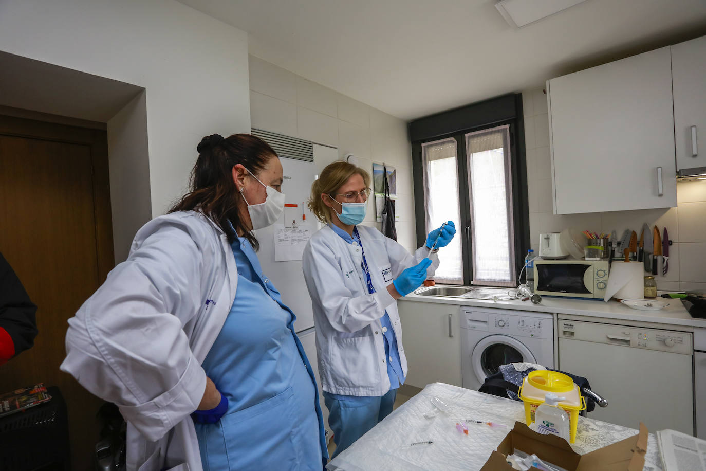 Las sanitarias preparan la dosis para Unai en la cocina de su casa. El preparado comparte mesa con un ejemplar de EL CORREO y una barra de pan recién comprada. 