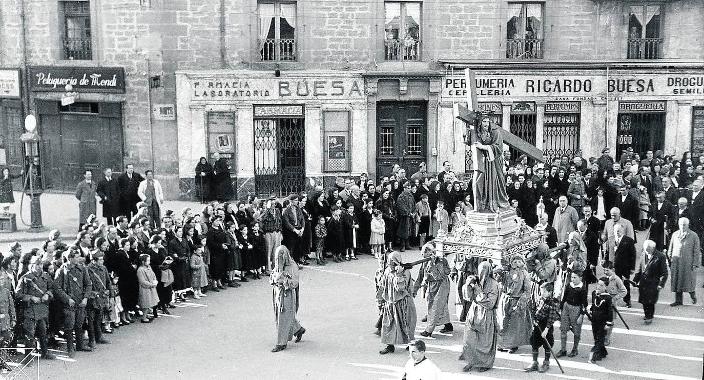 El 2 de abril de 1926, Viernes Santo, salió por primera vez a las calles de Vitoria ‘Jesús con la Cruz a Cuestas’, también conocido como ‘Jesús, camino del Calvario’, en la procesión del Santo Entierro o Santo Sepulcro desde la parroquia de San Vicente Mártir. La talla fue bien acogida por los fieles que la esperaban en el centro de la ciudad. Bienvenida no solo por ocupar el vacío del ‘Nazareno’ que se veneraba en la capilla de los Pasos, retirada de la procesión por su deterioro, sino porque el estreno del Crucificado añadía otro aliciente a una marcha religiosa que recobraba esplendor y admiración. El empeño del párroco de San Vicente Florentino Bastida y de las cofradías en ella asentadas -la Cruz Enarbolada, La Dolorosa y el Santo Sepulcro- hizo posible la escultura de madera elaborada en los talleres Río de Barcelona, cuyas andas talló el carpintero local Román Goicoechea. Costó apenas 3.000 pesetas que se reunieron gracias a una aportación del Ayuntamiento y a limosnas de feligreses. Con una altura de 1,70 metros, la figura representa a Jesucristo arrastrando, sudoroso y cansino, el pesado madero, cubierto con una túnica que realza sus pliegues. La foto muestra el paso llevado por cofrades el Viernes Santo de 1935, 19 de abril, en la hoy esquina Diputación-Prado, hacia la plaza General Loma. En la actualidad sigue procesionándose.