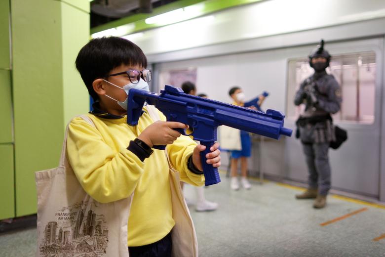 Los niños juegan con pistolas de juguete junto a un miembro del equipo de respuesta ferroviaria en un modelo de una estación de ferrocarril de tránsito masivo (MTR) durante una jornada de puertas abiertas .