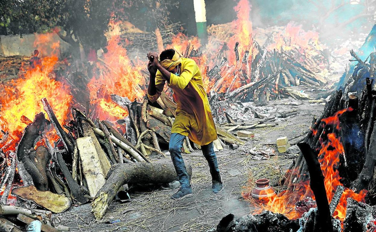 Un hombre pasa corriendo junto a las piras funerarias de víctimas de coronavirus durante una cremación masiva en Nueva Delhi.